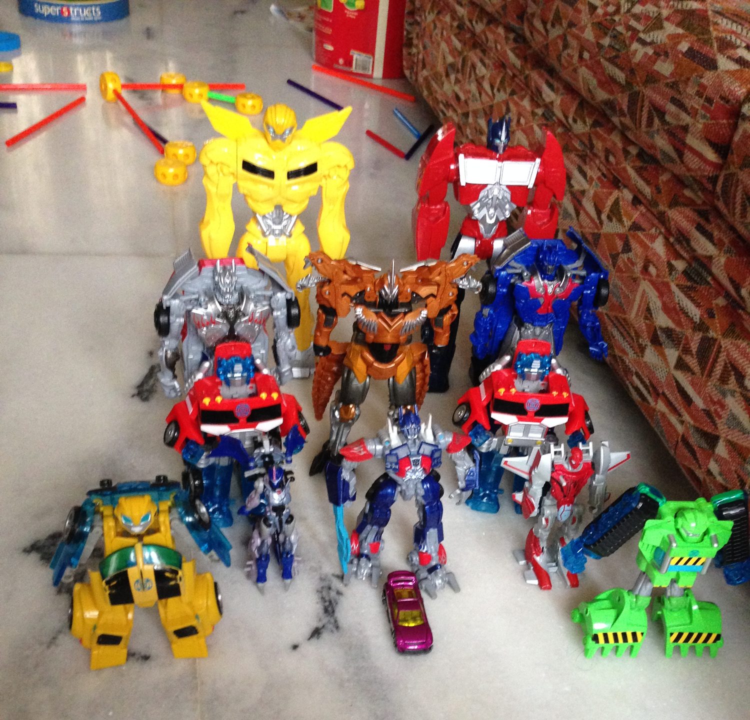 A dozen Transformers figures arranged in rows on a marble floor.